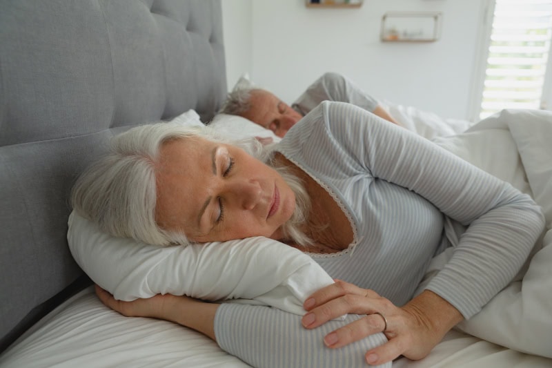 3 Benefits For Using Your AC While Sleeping. Senior couple sleeping together in their bed.