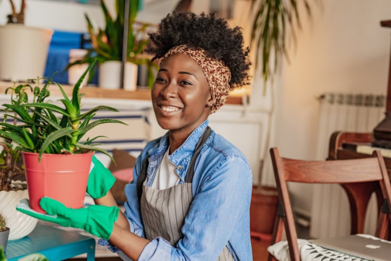 African woman taking care of plants at her home, she is holding a plant and smiling.