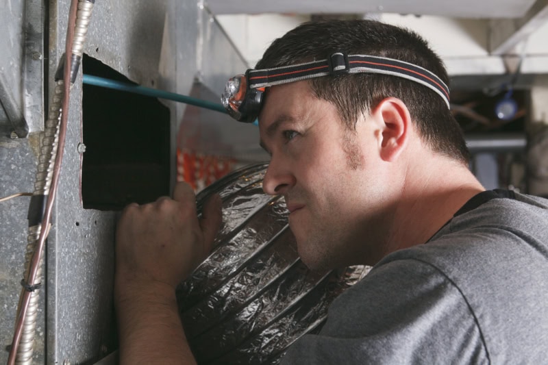 Why Is My Furnace Leaking Water? Photo of a maintenance worker inspecting an air vent.