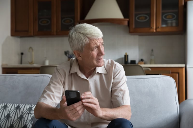 What’s That Smell Coming From My Furnace? Photo of a senior man sitting on his couch, looking outside while on his phone, seemingly worried.