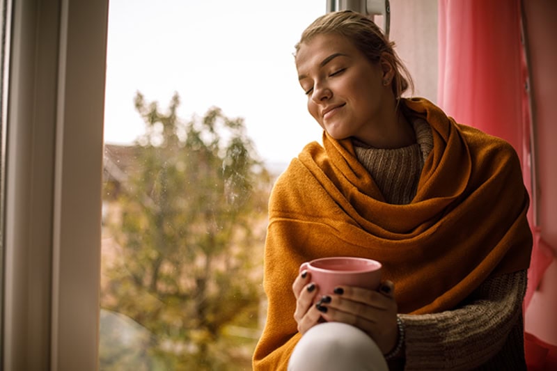woman sitting against a window, looking cozy, fall background.